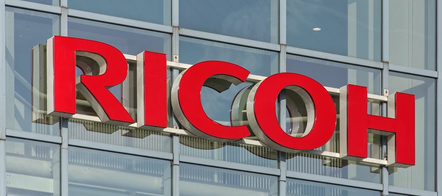 Insegna RICOH su edificio moderno, da startup a marchio globale di stampanti.