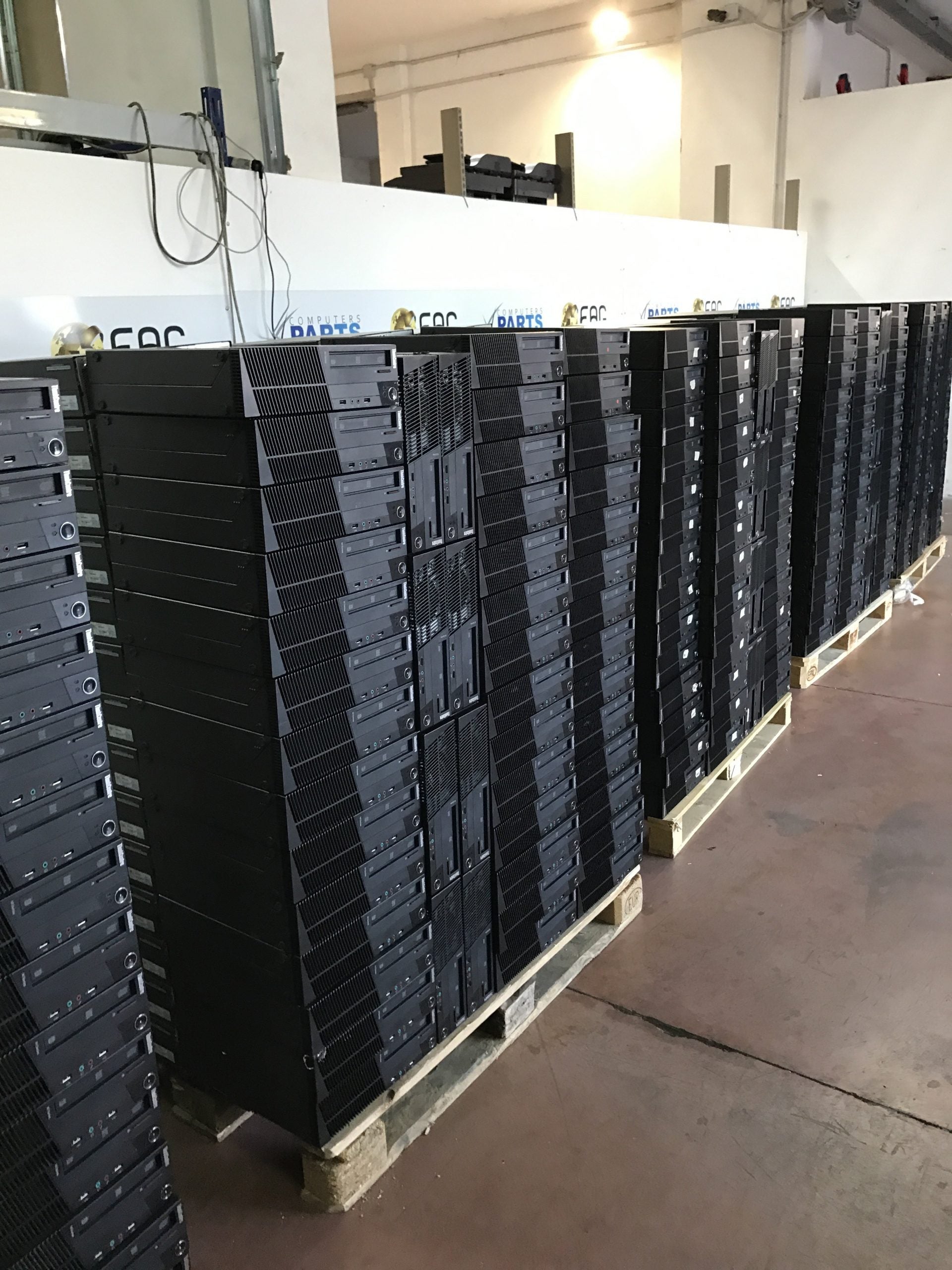 Numerosi pc desktop ricondizionati impilati su pallet in magazzino Messoanuovo.it.