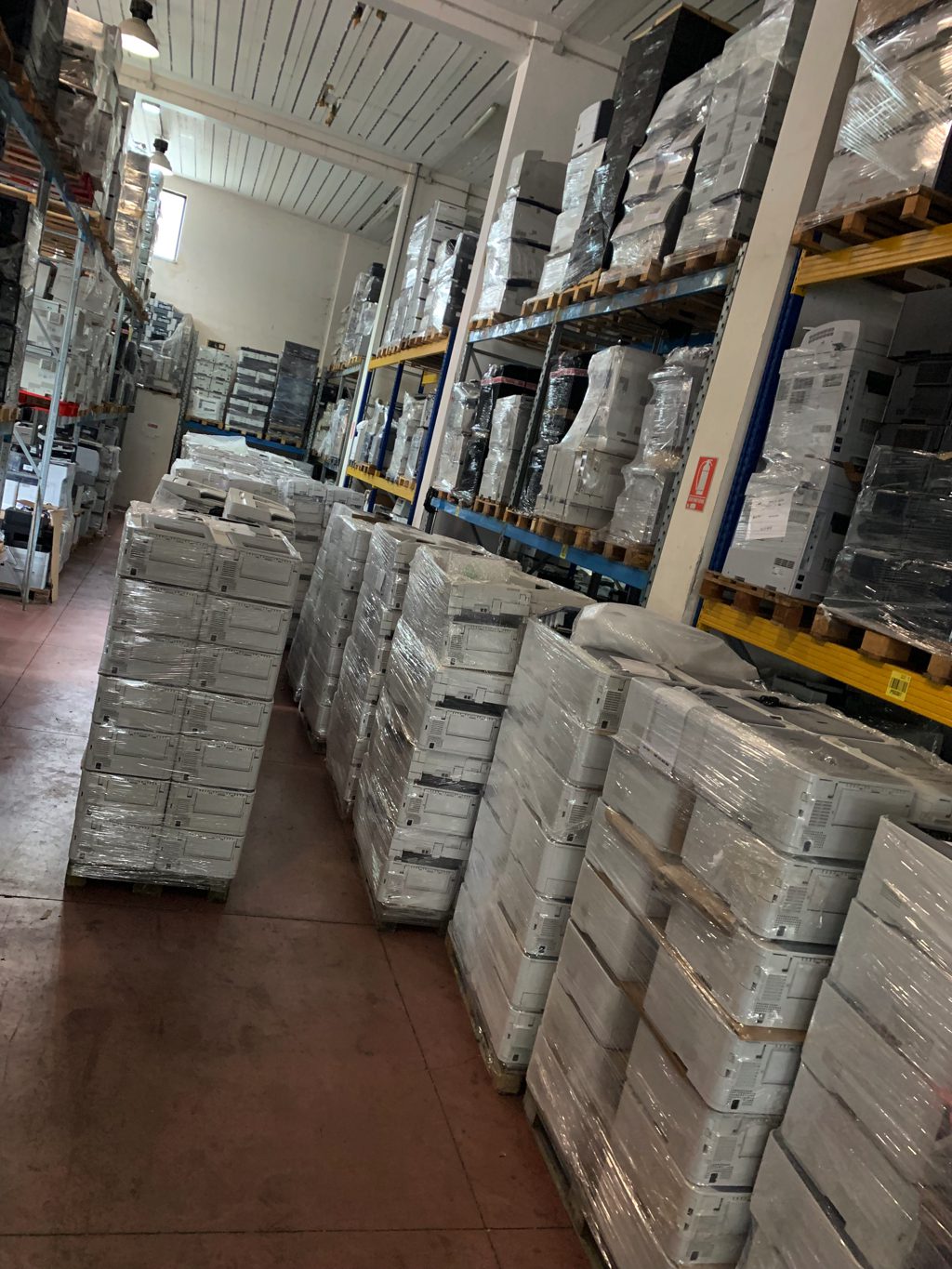 Magazzino Messoanuovo.it con stampanti ricondizionate e multifunzione impilate su pallet